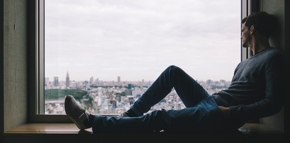 Man sitting in a window looking out at the city